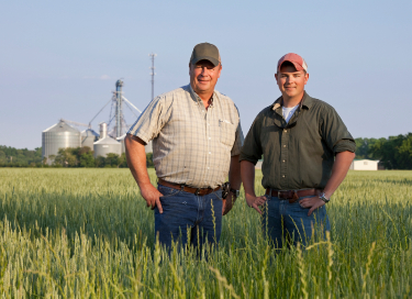 father and son standing in front of farm